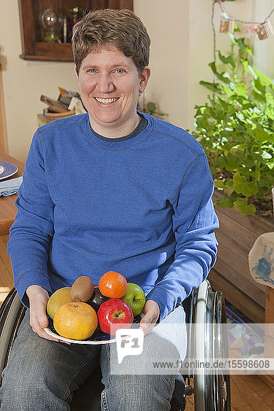 Porträt einer Frau mit Multipler Sklerose im Rollstuhl  die einen Teller mit Früchten hält