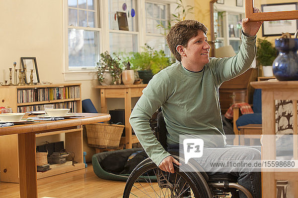 Frau mit Multipler Sklerose im Rollstuhl holt Tischdecken aus einem zugänglichen Schrank