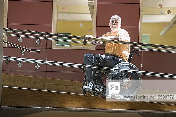 Seitenprofil eines Mannes mittleren Alters mit Muskeldystrophie  der in einem Rollstuhl auf einer Rollstuhlrampe sitzt