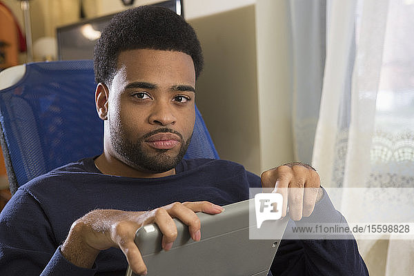 Afroamerikanischer Mann mit zerebraler Lähmung hält sein Tablet zu Hause