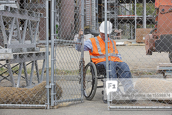 Projektingenieur mit einer Rückenmarksverletzung im Rollstuhl  der den Zaun zur Baustelle schließt