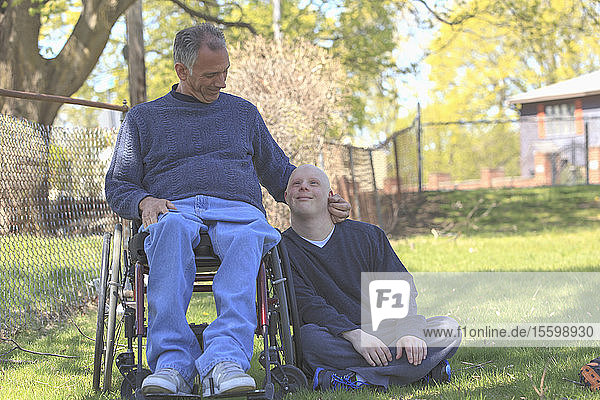 Glücklicher Vater mit Rückenmarksverletzung und sein Sohn mit Down-Syndrom in einem Park
