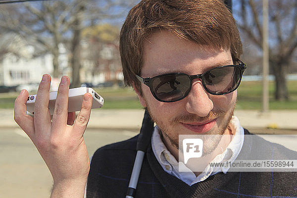 Junger blinder Mann in seiner Nachbarschaft  der mit seinem Mobiltelefon Hilfsmittel benutzt
