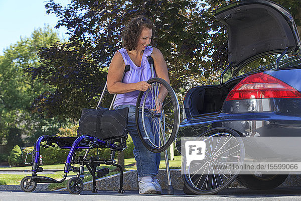 Frau mit Spina Bifida benutzt Krücken  um den Rollstuhl für die Fahrt im Auto zu zerlegen