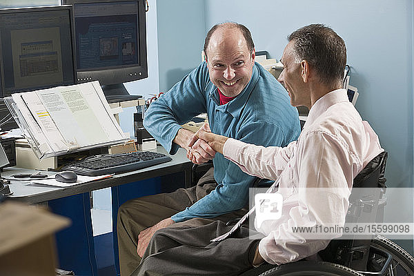 Two businessmen shaking hands in an office one with Friedreich's Ataxia and another with spinal cord injury