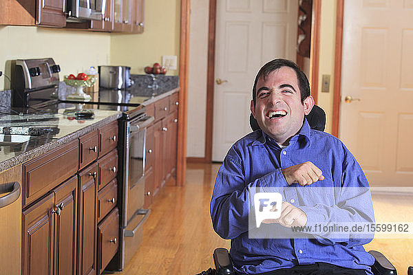 Mann mit Cerebralparese in seinem motorisierten Rollstuhl lacht in seiner Küche