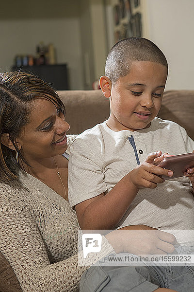 Hispanic boy with Autism playing an electronic game with his mother at home