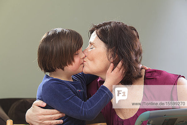 Kleines Mädchen mit Down-Syndrom küsst ihre Mutter