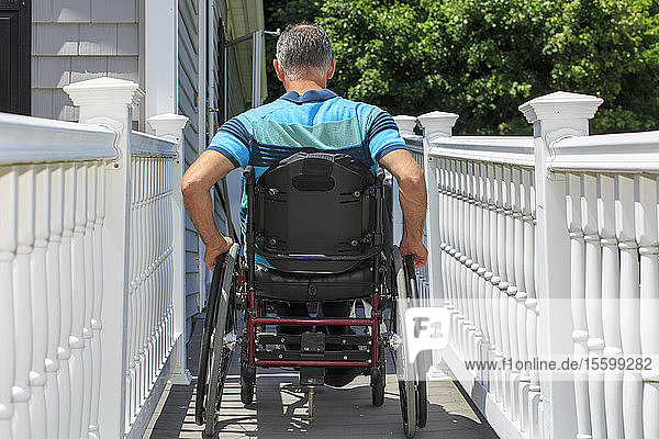Ein Mann mit einer Rückenmarksverletzung im Rollstuhl fährt die Rampe seines Hauses hoch