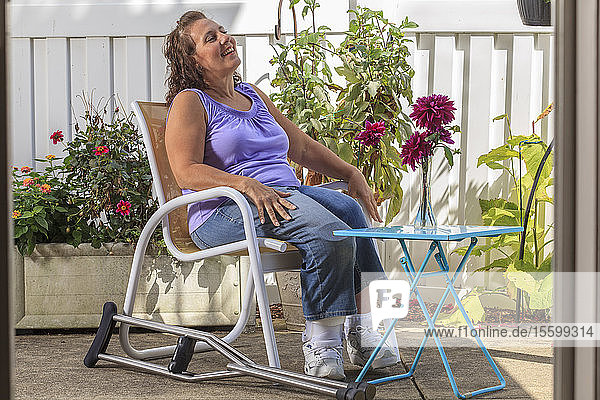 Frau mit Spina Bifida entspannt sich auf einer Gartenterrasse