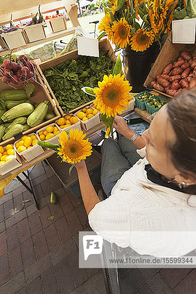 Frau mit Querschnittslähmung sitzt im Rollstuhl und kauft auf einem Markt für Sonnenblumen ein