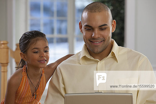 Hispanic man working on a laptop with his daughter beside him