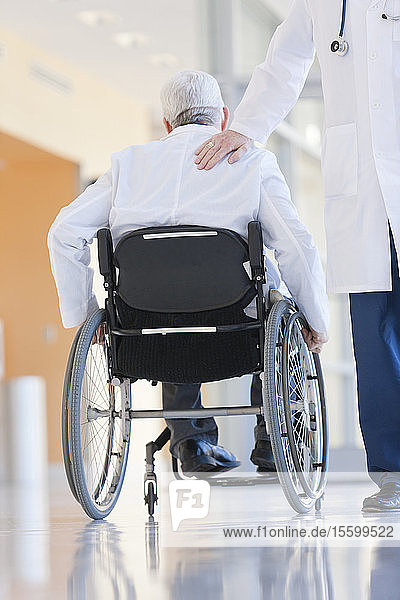 Arzt klopft einem anderen auf die Schulter  der mit Muskeldystrophie im Rollstuhl sitzt