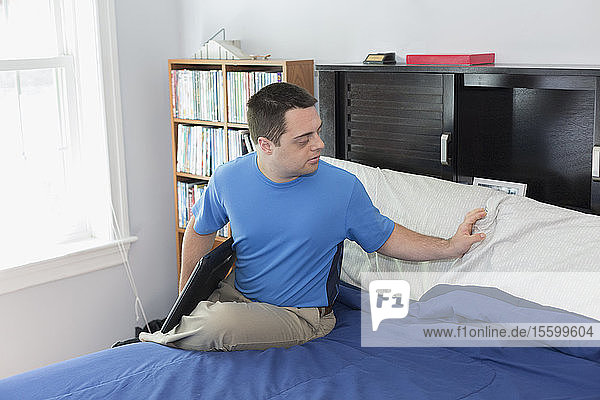Mann mit Down-Syndrom sitzt auf einem Bett und hält einen Laptop