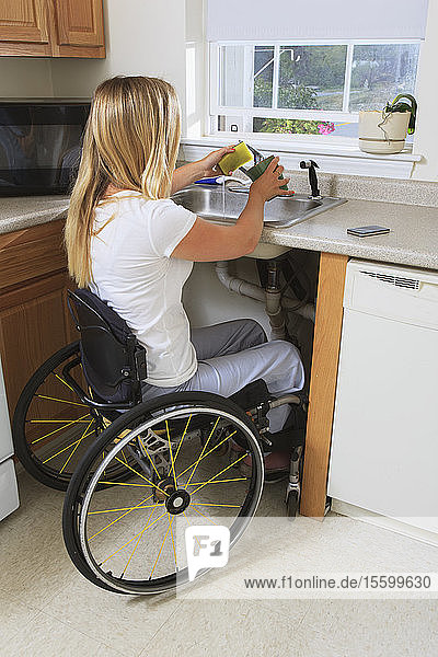 Frau mit Rückenmarksverletzung in ihrer barrierefreien Küche beim Geschirrspülen