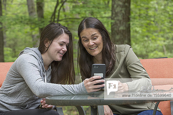 Glückliche Frau mit Multipler Sklerose schaut mit ihrer Tochter auf ein Telefon