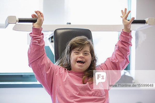Junge Frau mit Down-Syndrom bei der Arbeit an einem Trainingsgerät im Fitnessstudio