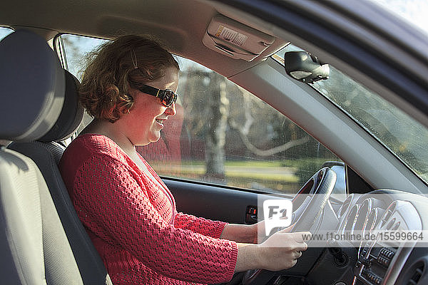 Junge Frau mit Autismus sitzt auf dem Fahrersitz ihres Autos