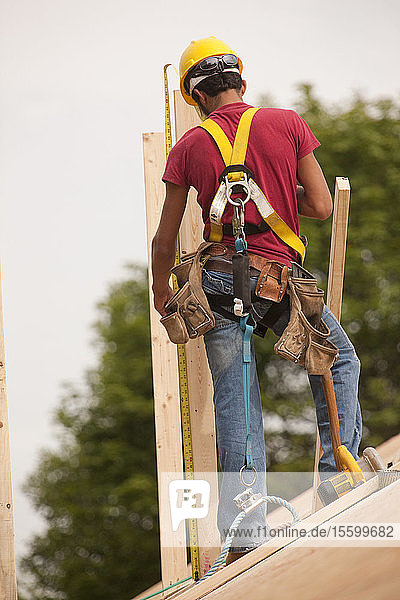 Ein spanischer Zimmermann misst ein Brett auf dem Dach eines im Bau befindlichen Hauses aus
