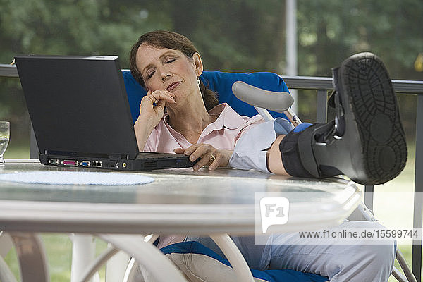 Woman with a boot on her foot napping on a chair in front of a laptop