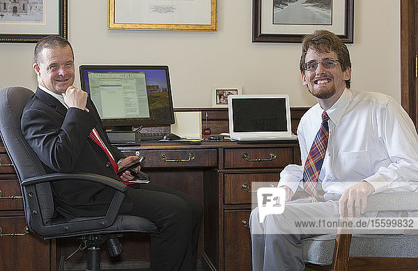 Man with Down Syndrome smiling with a collaborator in the State Capitol in his office