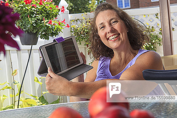 Frau mit Spina Bifida arbeitet auf der Terrasse an einem Tablet
