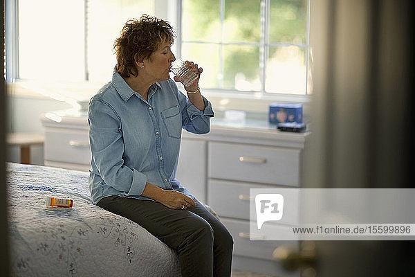 Reife Frau trinkt Wasser  um ihre Tabletten herunterzuspülen
