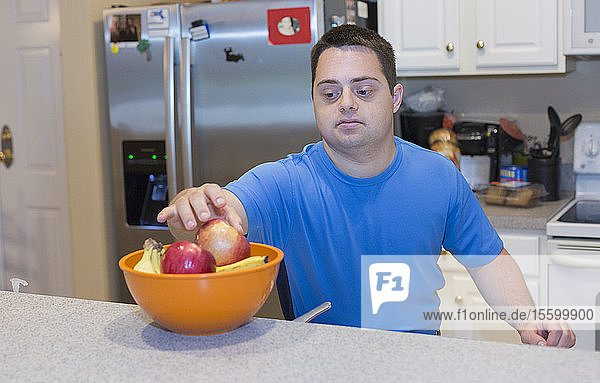 Mann mit Down-Syndrom steht in der Küche und hält Obst