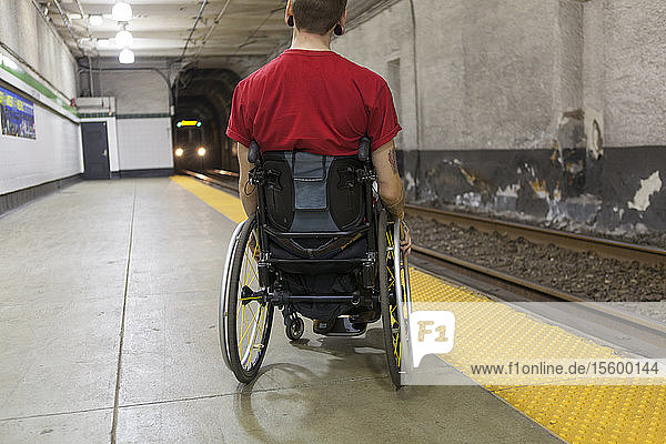 Trendiger Mann mit einer Rückenmarksverletzung im Rollstuhl  der auf einen U-Bahn-Zug wartet