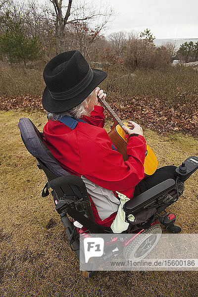Mann mit Multipler Sklerose in einem motorisierten Rollstuhl genießt seinen Garten mit seiner Gitarre