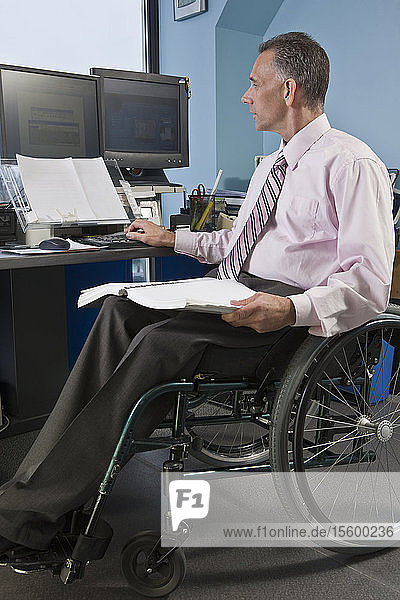Geschäftsmann mit Querschnittslähmung im Rollstuhl bei der Arbeit in einem Büro