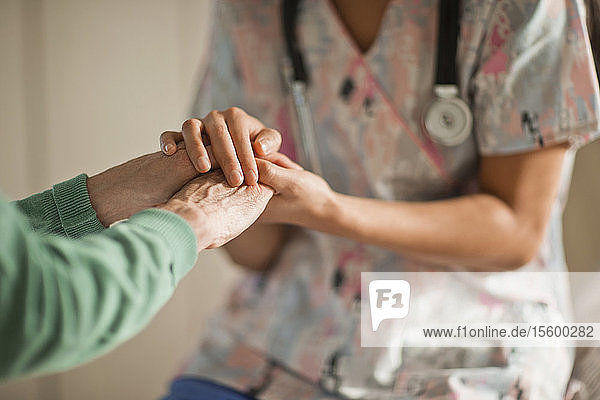 Junge Krankenschwester hält die Hände einer älteren Frau.