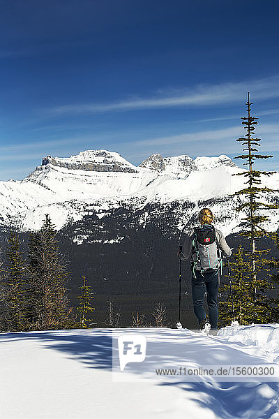 Female hiker on snow-covered pathway with snow-covered mountains  blue sky and clouds in the background; Lake Louise  Alberta  Canada