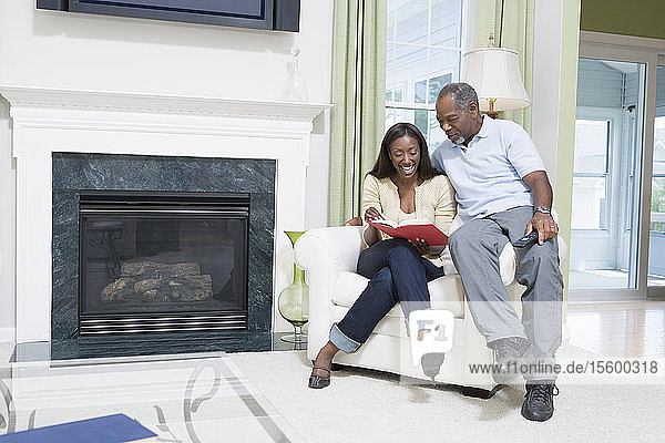 Ehepaar mittleren Alters sitzt in einem Sessel  schaut in ein Buch und lächelt