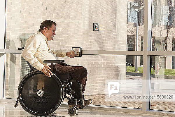 Geschäftsmann mit Querschnittslähmung im Rollstuhl benutzt den automatischen Türöffner am Eingang eines Bürogebäudes