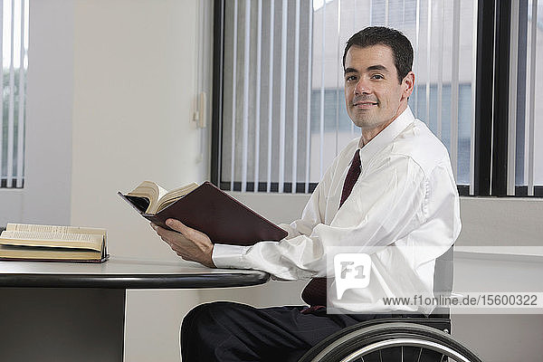 Geschäftsmann mit Rückenmarksverletzung hält ein Buch und lächelt