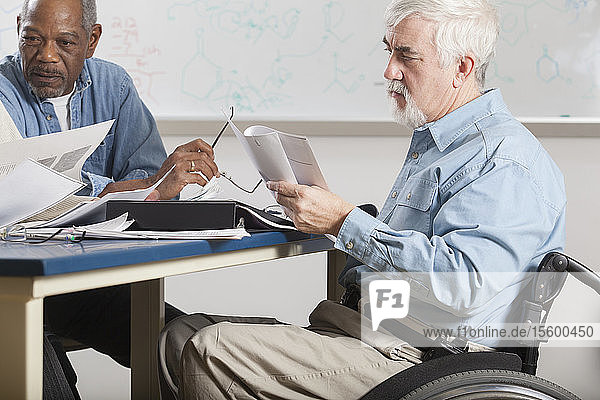 Professor mit Muskeldystrophie in einem Rollstuhl bei einer Fakultätssitzung