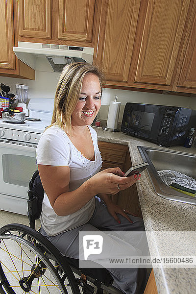 Woman with spinal cord injury in her accessible kitchen using a mobile phone
