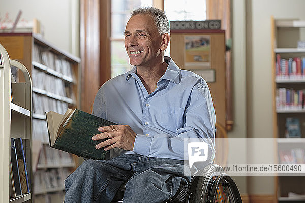 Mann im Rollstuhl mit einer Rückenmarksverletzung genießt ein Buch in einer Bibliothek