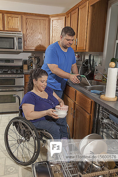 Frau mit Spina Bifida und ihr Mann benutzen den Geschirrspüler in der Küche