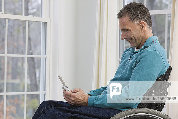 Mann sitzt im Rollstuhl und benutzt einen persönlichen Datenassistenten