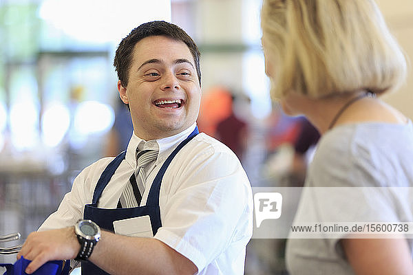 Mann mit Down-Syndrom arbeitet in einem Lebensmittelladen und begrüßt einen Kunden