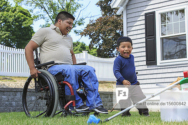 Hispanischer Mann mit Rückenmarksverletzung im Rollstuhl und sein Sohn bereiten sich auf das Waschen eines Autos vor