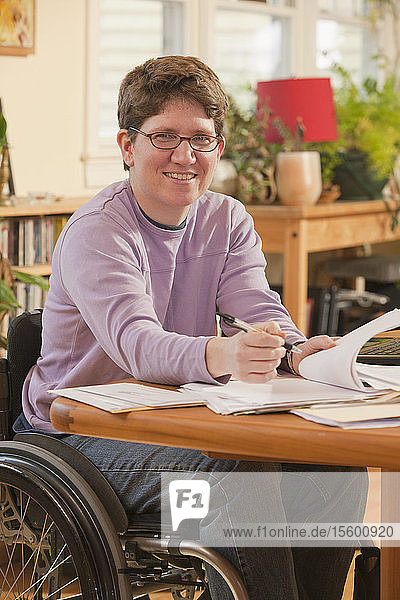 Geschäftsfrau mit Multipler Sklerose im Rollstuhl erledigt Papierkram zu Hause