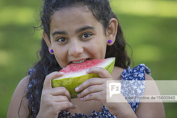 Porträt eines glücklichen hispanischen Teenagers mit Zahnspange  der eine Wassermelone isst