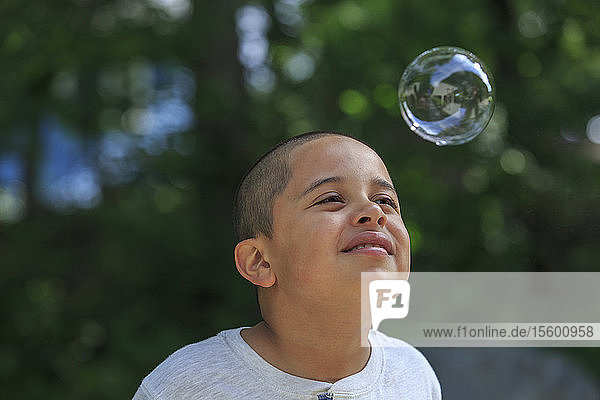 Glücklicher hispanischer Junge mit Autismus spielt mit einer Seifenblase im Park