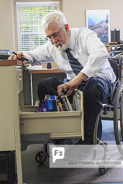 Man with Muscular Dystrophy in a wheelchair taking files of information from his desk drawer