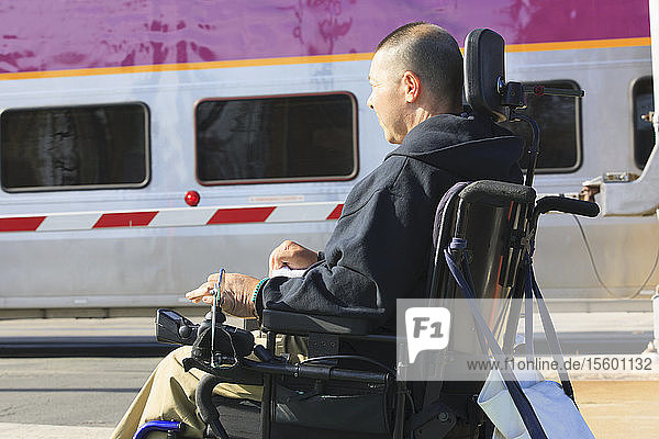 Mann mit Rückenmarksverletzung wartet mit seinem motorisierten Rollstuhl auf einen öffentlichen Zug