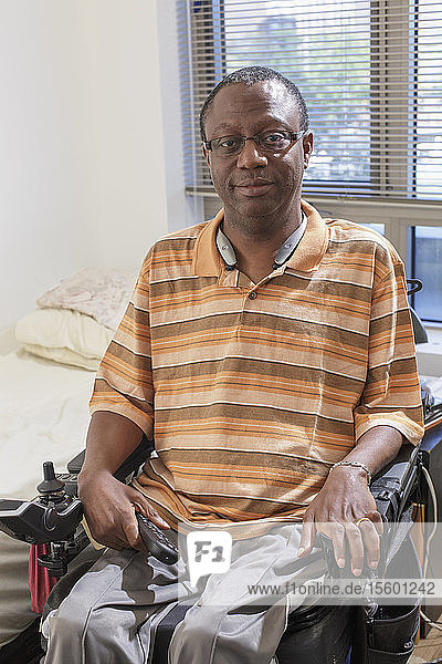 Mann mit Guillain-Barre-Syndrom  der in seinem elektrischen Rollstuhl zu Hause eine TV-Fernbedienung hält