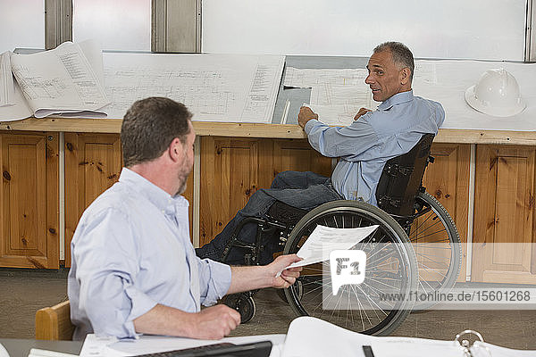Two project engineers doing paperwork about the job  one in a wheelchair with a Spinal Cord Injury